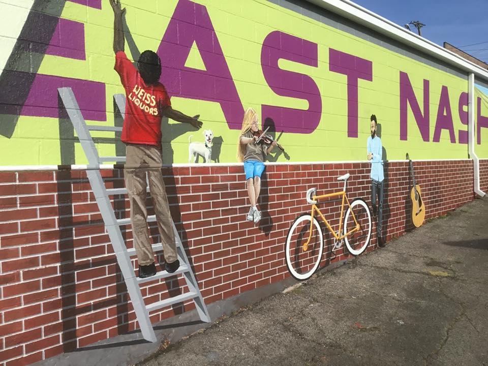 A man is painting a mural on the side of a building that says east nash