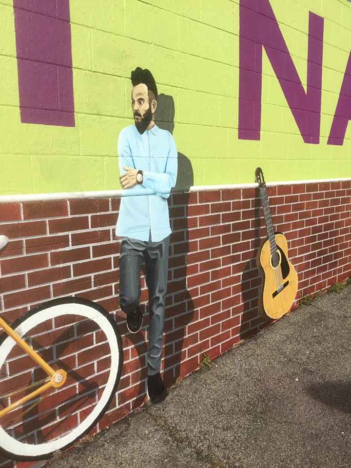 A man leaning against a brick wall next to a bicycle and a guitar