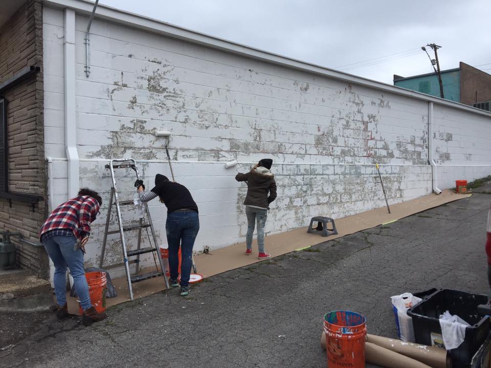 A group of people are painting a wall of a building.
