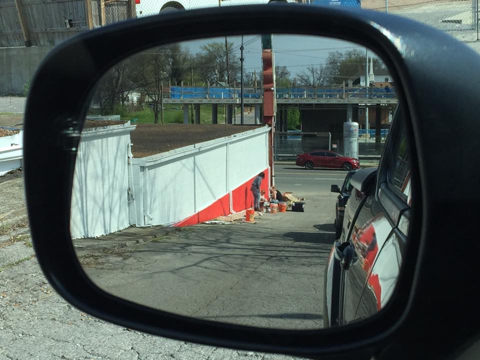 A rear view mirror shows a car parked on the side of the road