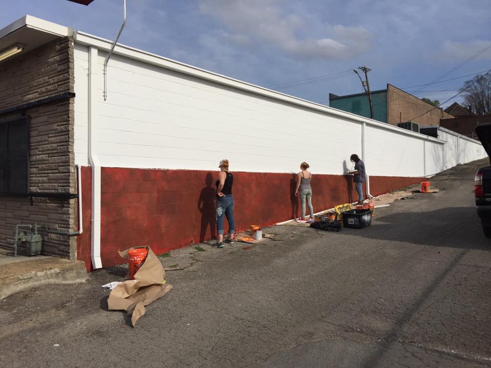 A group of people are painting a wall on the side of a building.