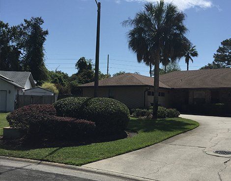 Residential house with driveway, landscaping, and palm trees under a blue sky.