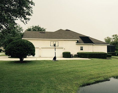 Side view of a light-colored house with a two-car garage, basketball hoop, and green lawn.