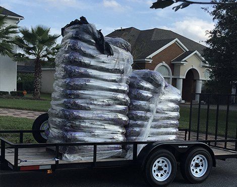 Trailer carrying several large, wrapped packages, possibly landscaping materials, in a residential neighborhood.