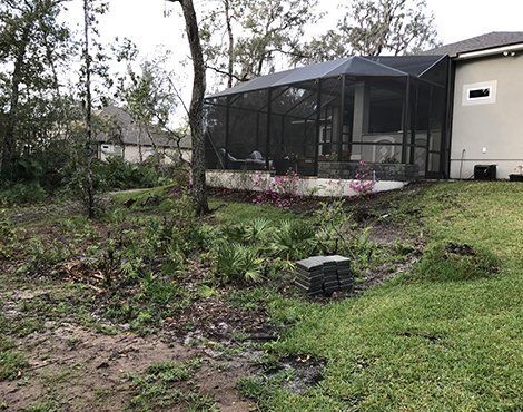 Backyard with screened porch, dirt patches, grass, and trees. Overcast sky.