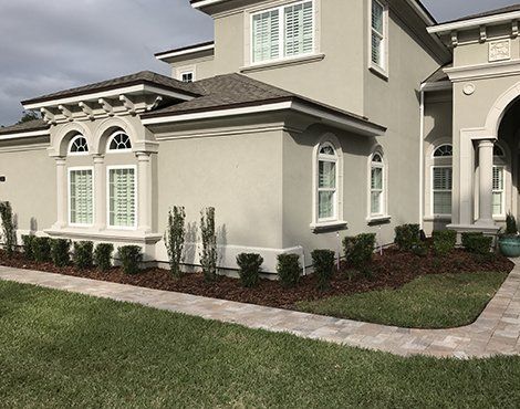 Exterior of a two-story beige stucco house with white trim, windows, and a landscaped yard.