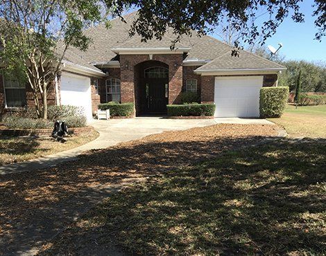 Brick house with a two-car garage, driveway, and landscaping on a sunny day.