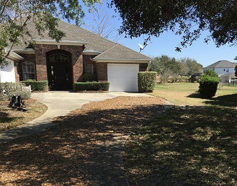 Brick house with arched doorway, attached garage, and driveway. Sunny day, green lawn.