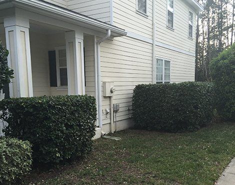 Exterior of a two-story beige house with bushes and a small patch of grass.