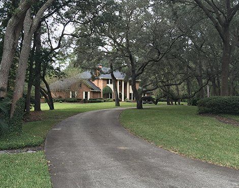 A long, curved driveway leads to a large brick house surrounded by trees and green grass.