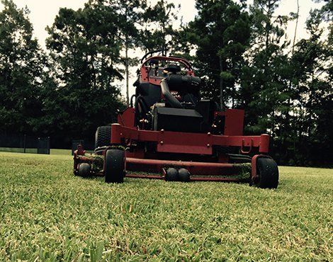Red commercial lawn mower on green grass, trees in the background.
