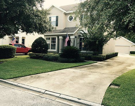 Beige two-story house with green lawn, driveway, and red truck in the yard, American flags, trees.
