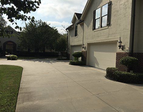 Concrete driveway leading to a two-car garage with cream-colored exterior. Lush green lawn on left.