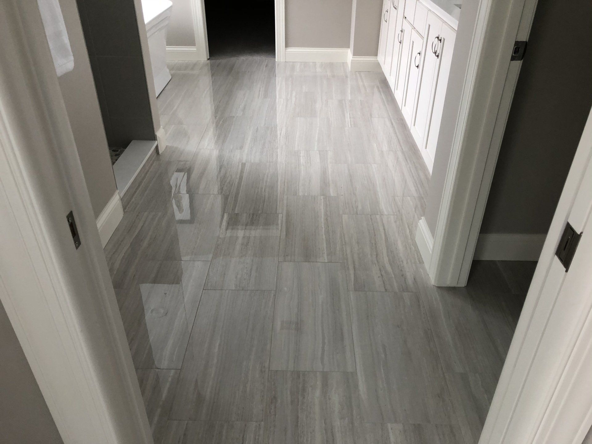A bathroom reconstruction with a gray tile floor and white cabinets.