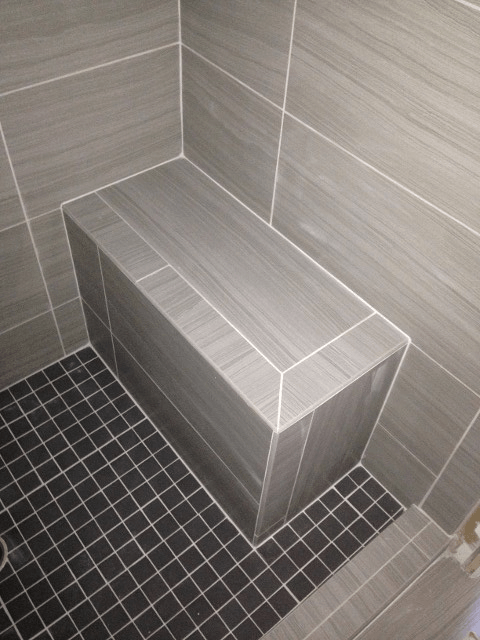 A tiled shower with a bench in the corner for elderly