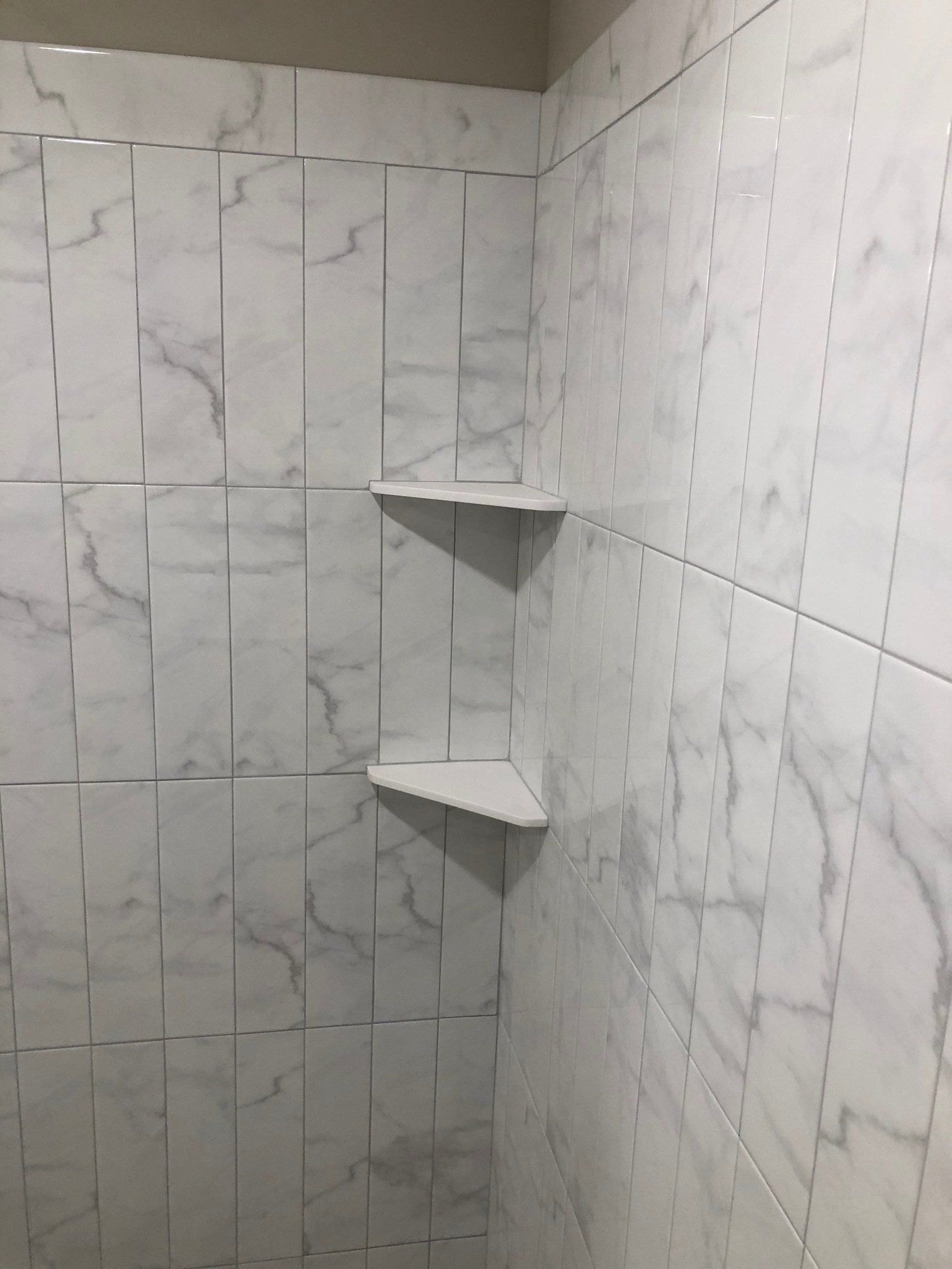 A shower with white tiles and shelves in the corner.