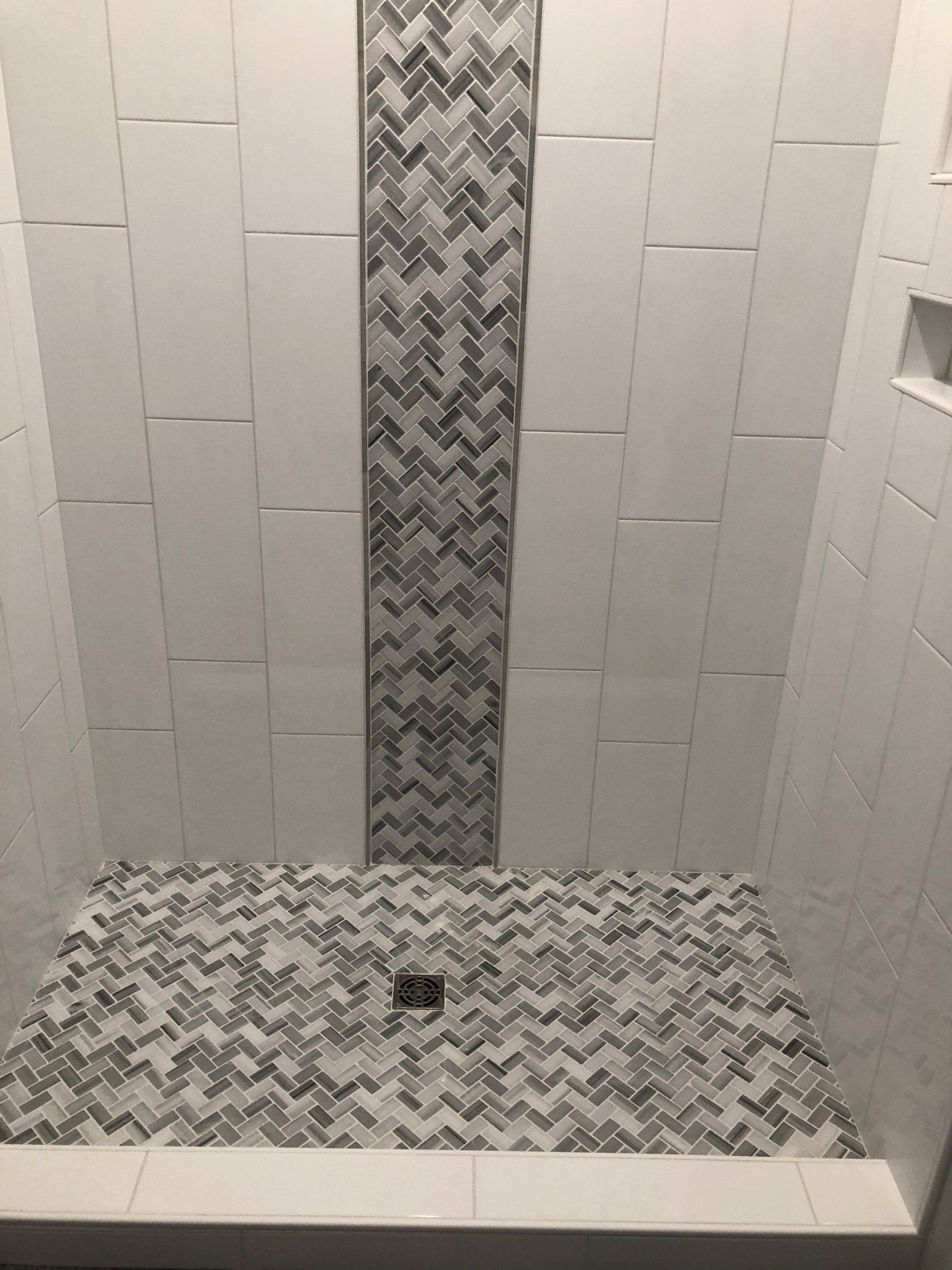 An upgraded shower with white tiles and a herringbone pattern on the floor.