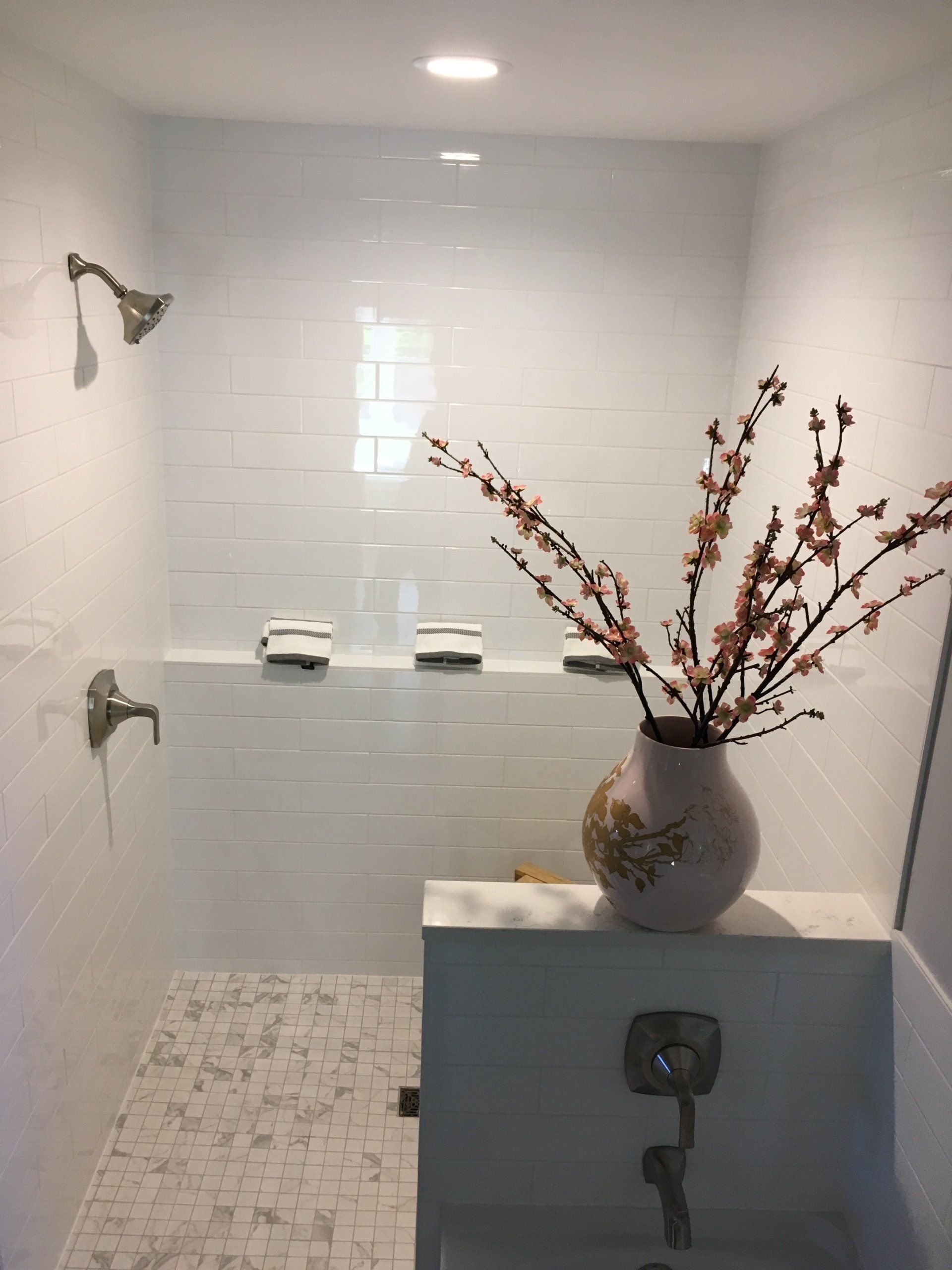 A renovated bathroom with white tiles and a vase with flowers in it