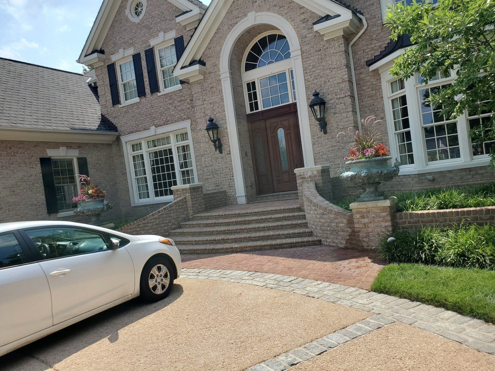 A white car is parked in front of a large brick house.