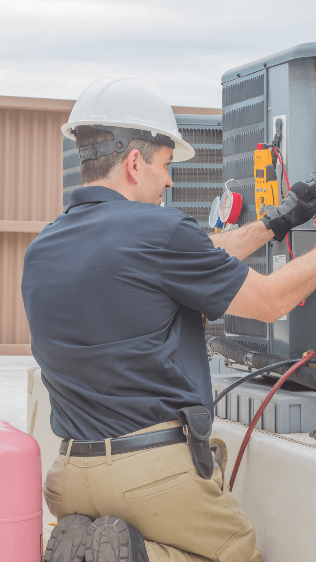 Technician in hard hat inspecting rooftop HVAC unit with tools and cables.