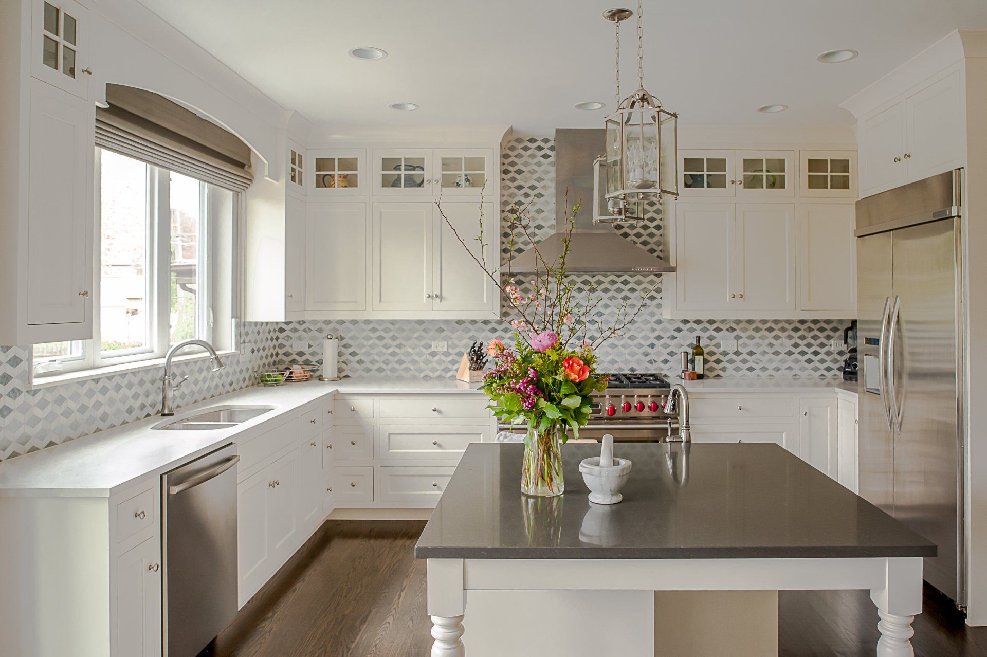 A kitchen with white cabinets , stainless steel appliances , and a large island with a vase of flowers on it.