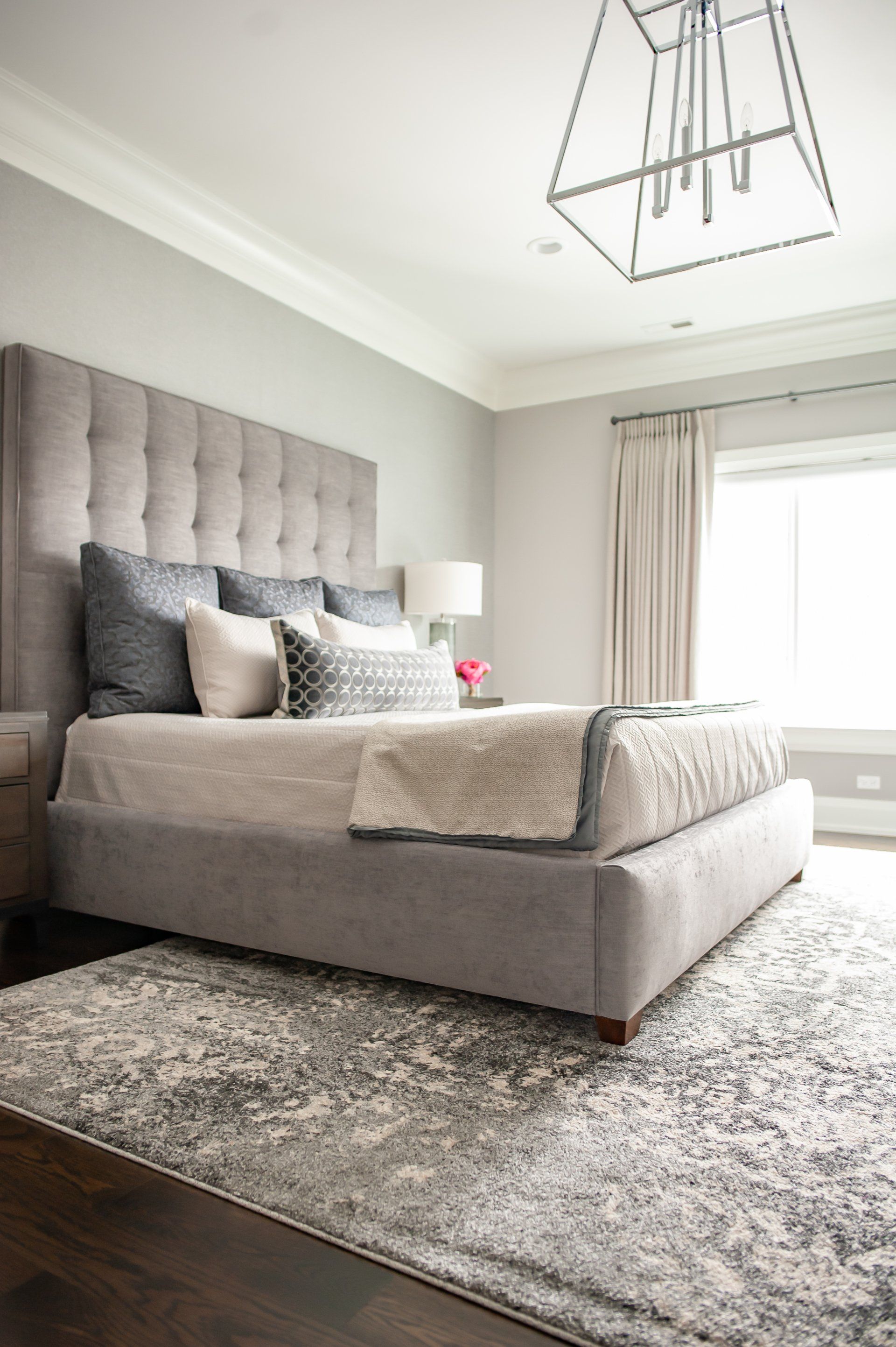 A bedroom with a bed , rug , window and chandelier.