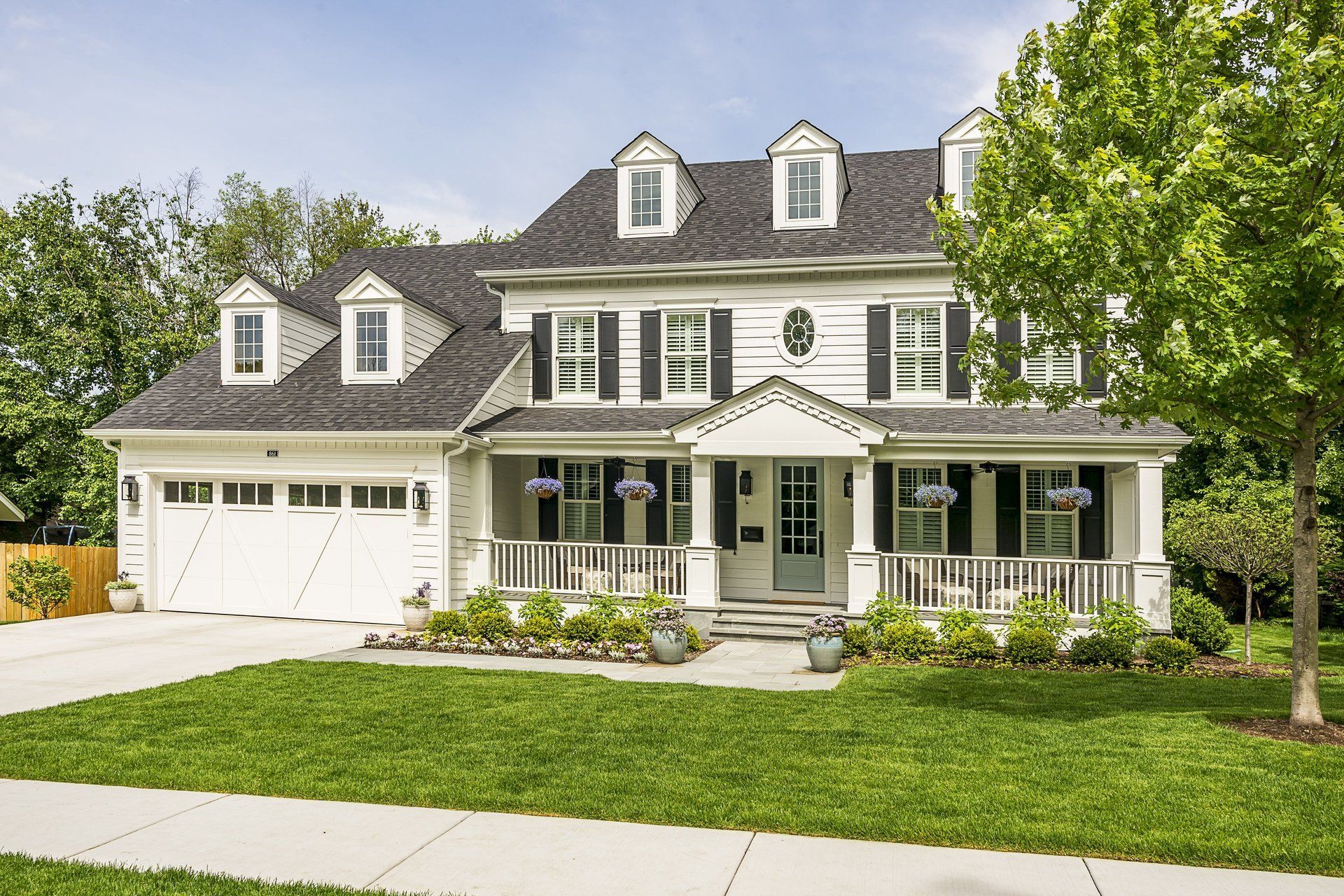 A large white house with black shutters is sitting on top of a lush green lawn.