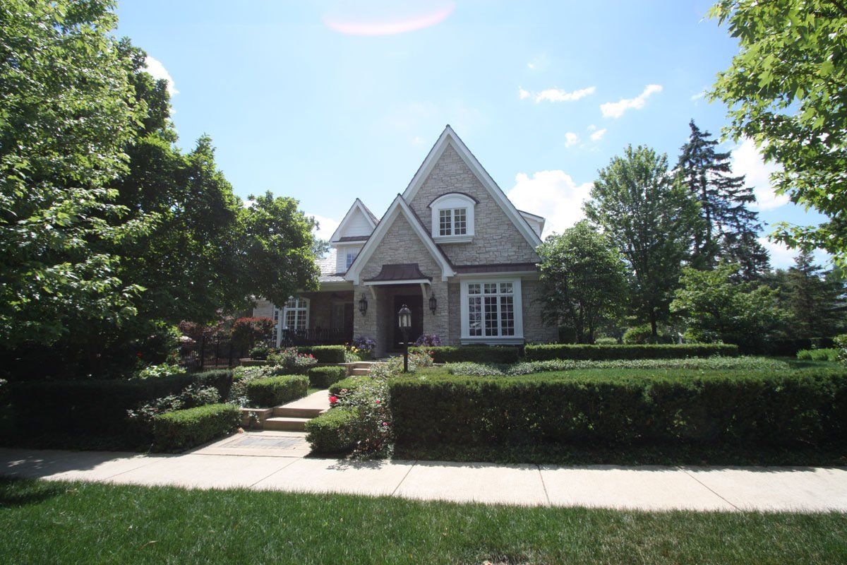 A large house is surrounded by trees and bushes on a sunny day