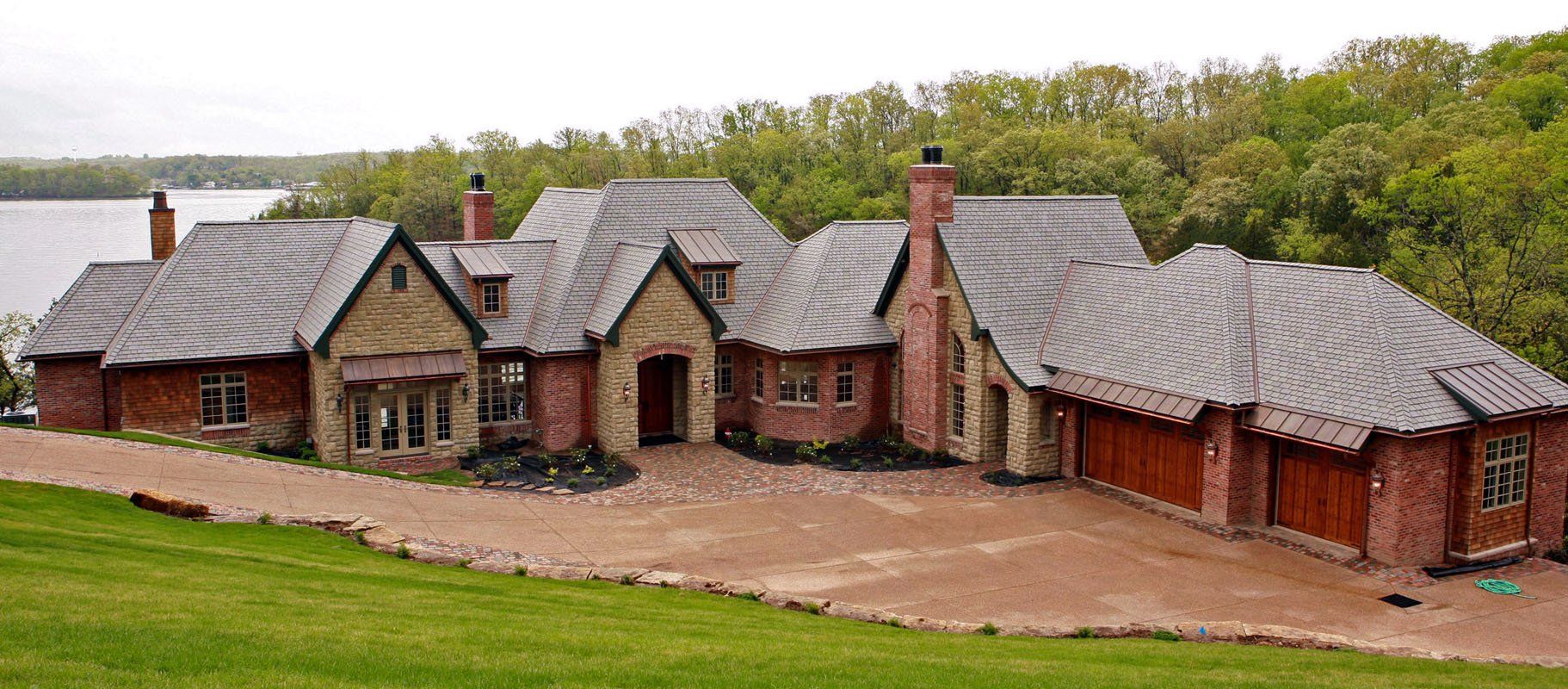 A large house is sitting on top of a hill next to a lake.
