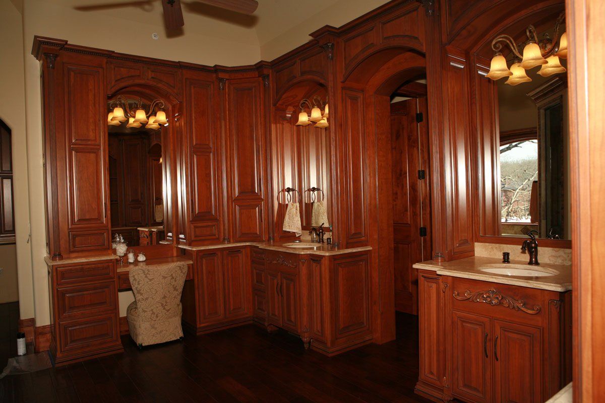 A bathroom with wooden cabinets , sinks , mirrors and a ceiling fan.