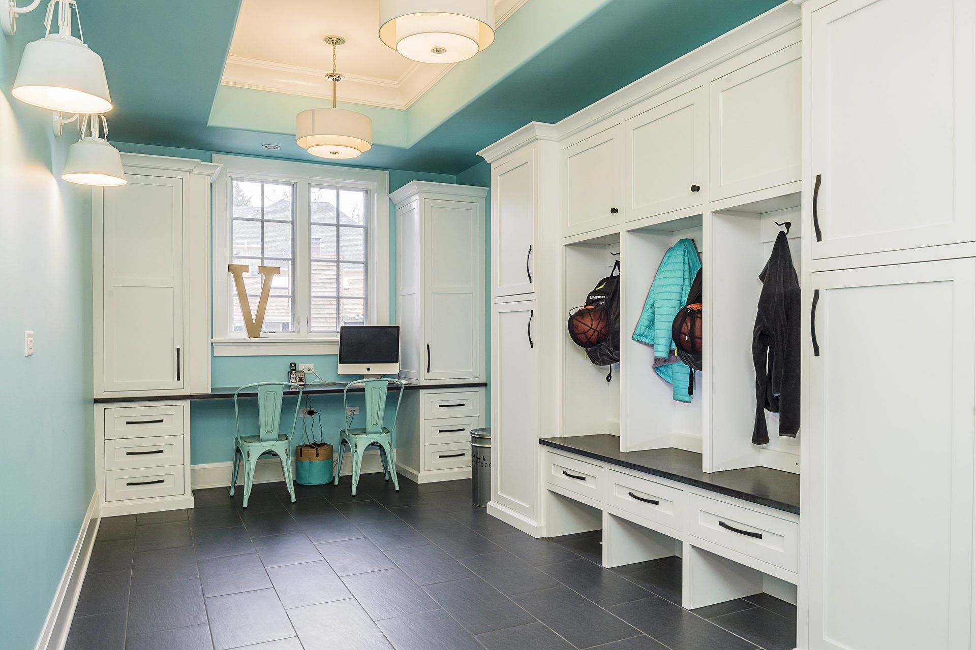 A room with a blue ceiling , white cabinets , a desk and chairs.
