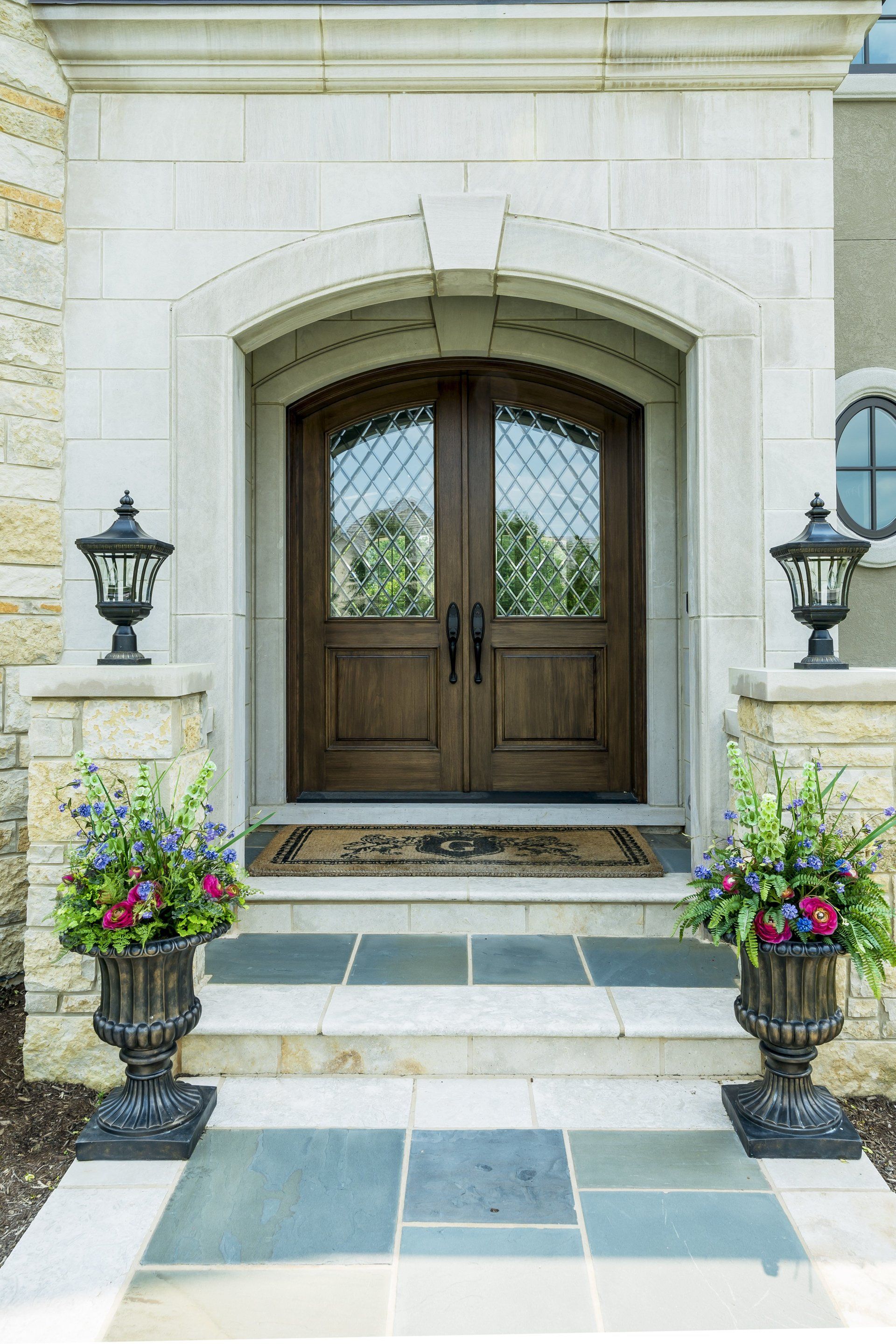 The front door of a house with two urns of flowers in front of it.