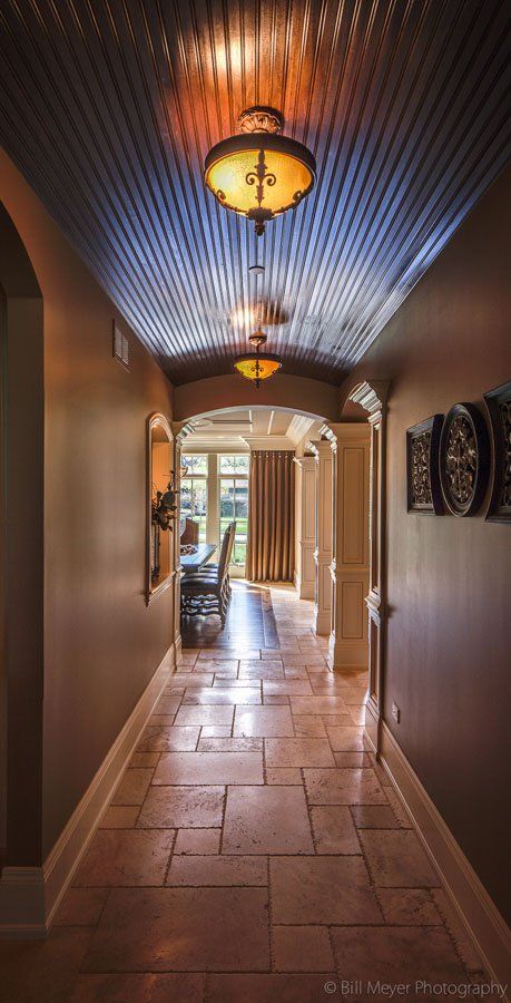 A long hallway with a tiled floor and a ceiling with lights hanging from it.