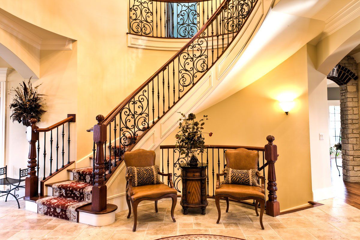 A staircase with a wrought iron railing and two chairs in front of it