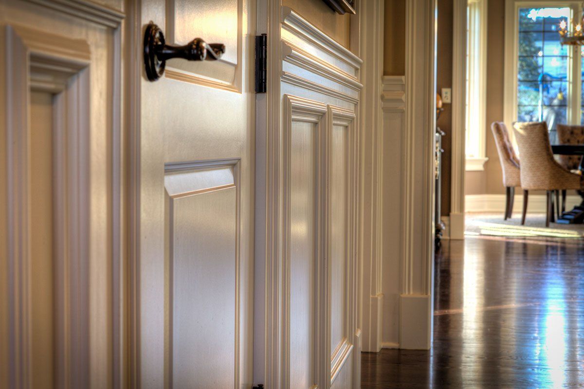 A hallway in a house with a door and a dining room in the background.