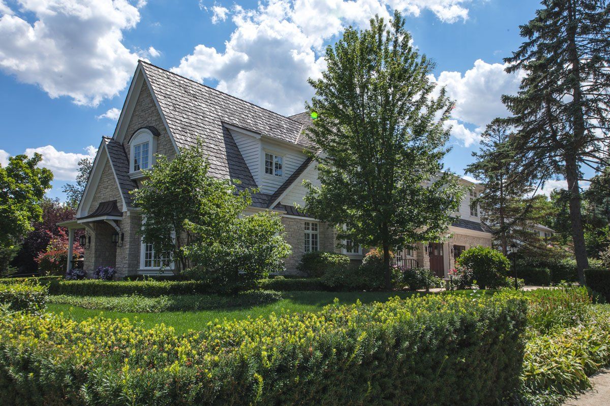 A large house is surrounded by trees and bushes on a sunny day.