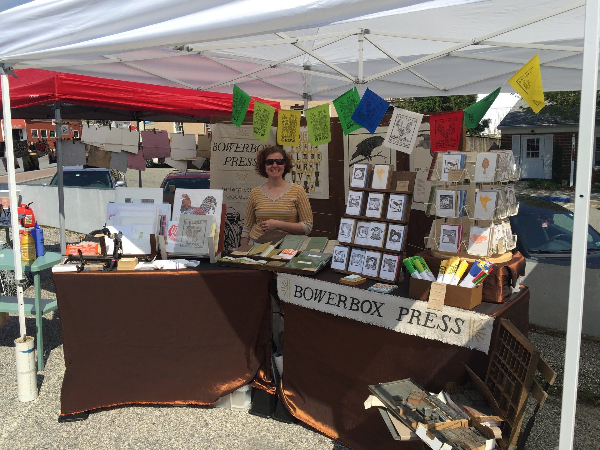 A woman is standing behind a table under a tent selling cards.