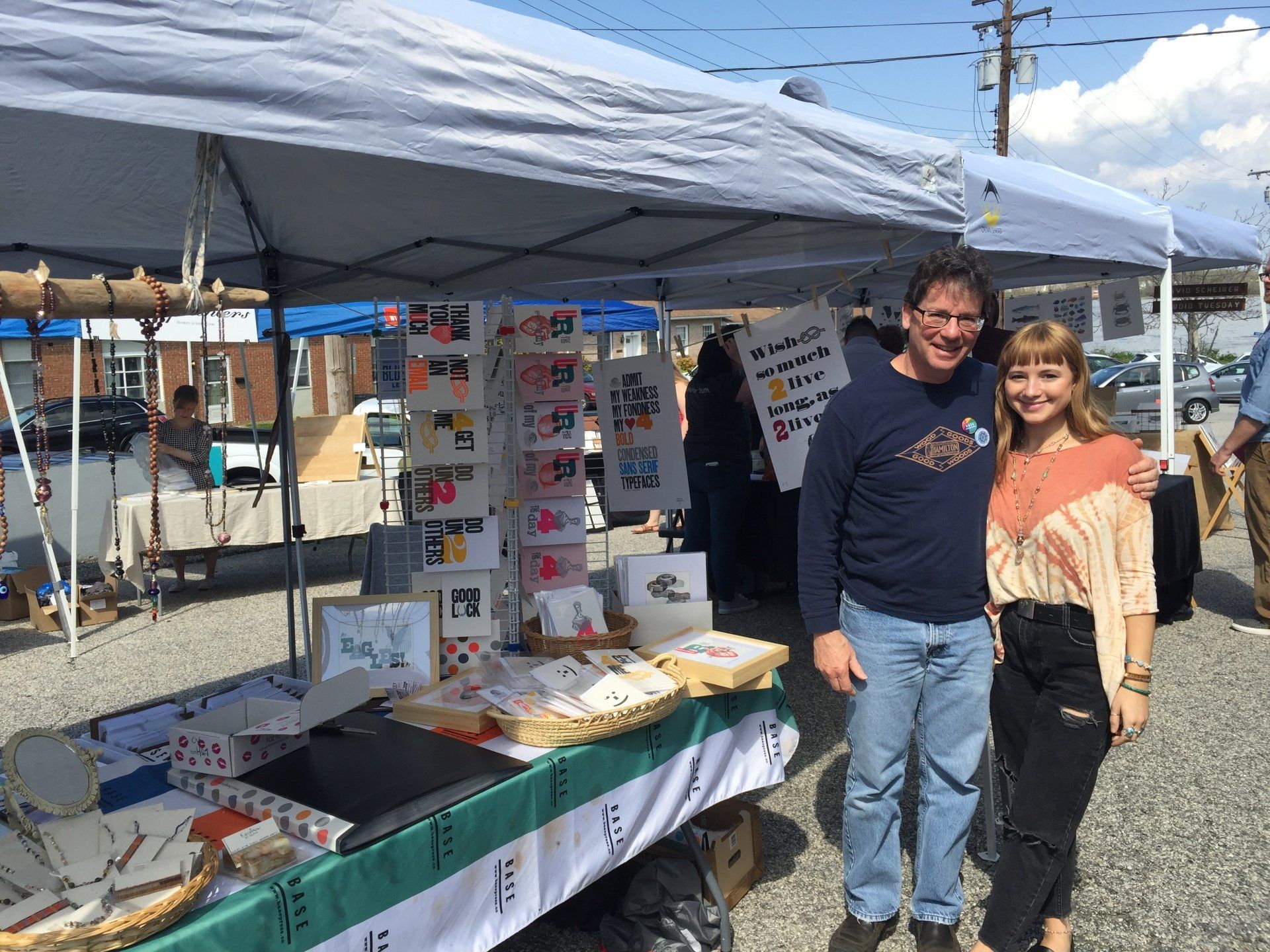 A man and a woman are standing in front of a tent at a market.