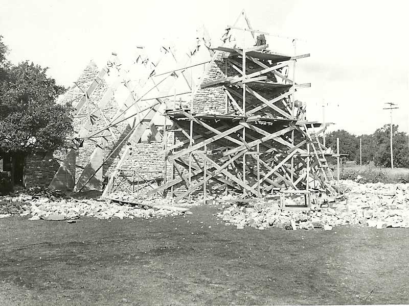 Church construction of  brick building with scaffolding, stones on the ground, trees in background.