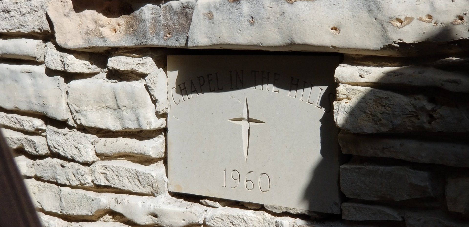 Stone wall with a cross etched into a rectangular stone, the year 1960 is below.