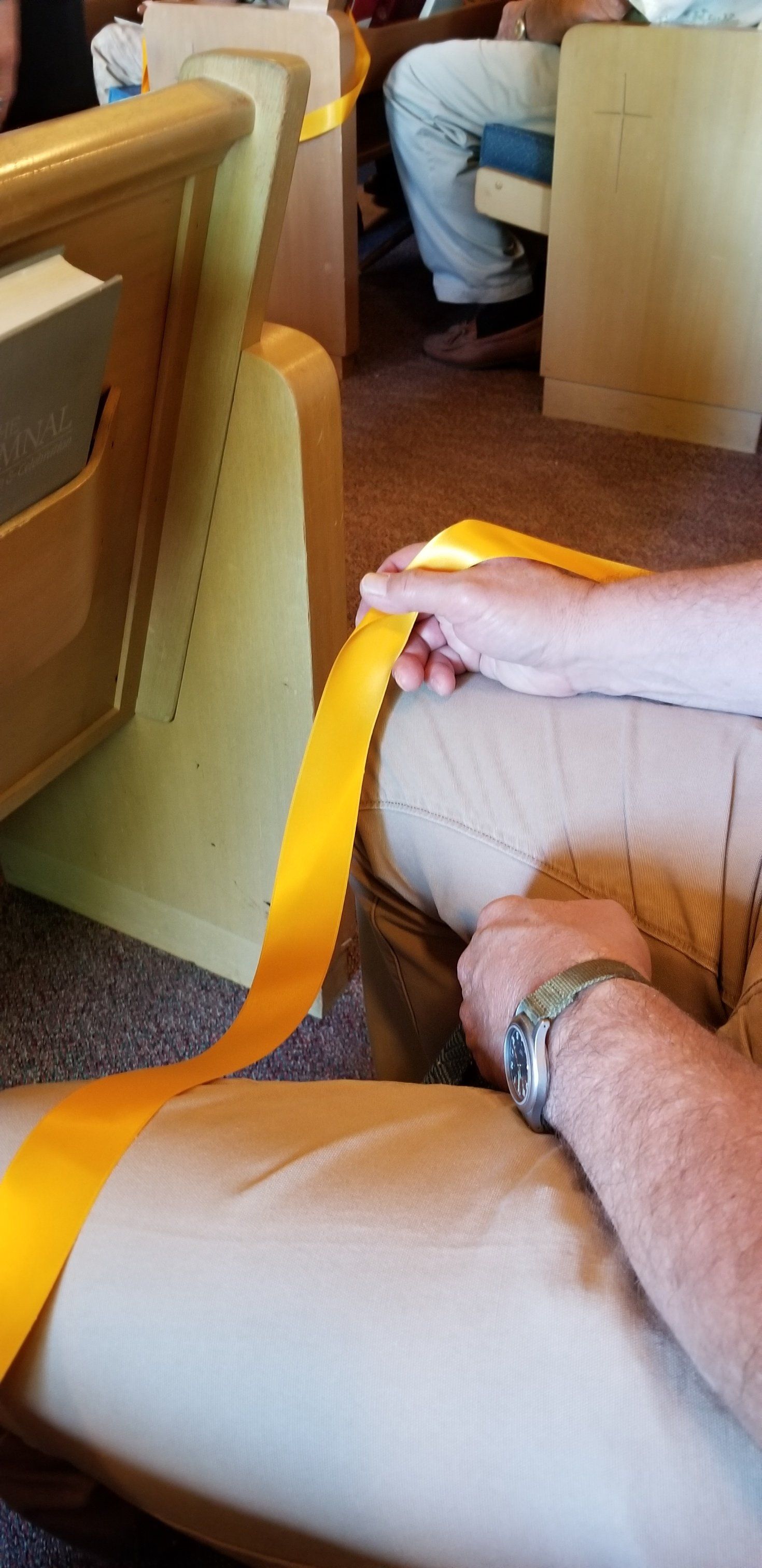 Person holding a long yellow ribbon in a pew, likely in a church or auditorium.