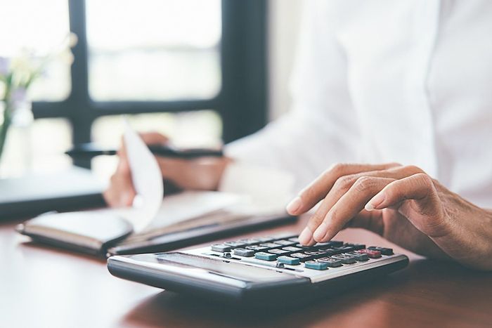 A person is typing on a calculator while holding a receipt.