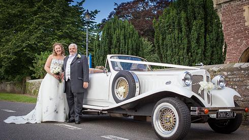 Spirit Wedding Cars | A bride and groom are standing next to a white car.