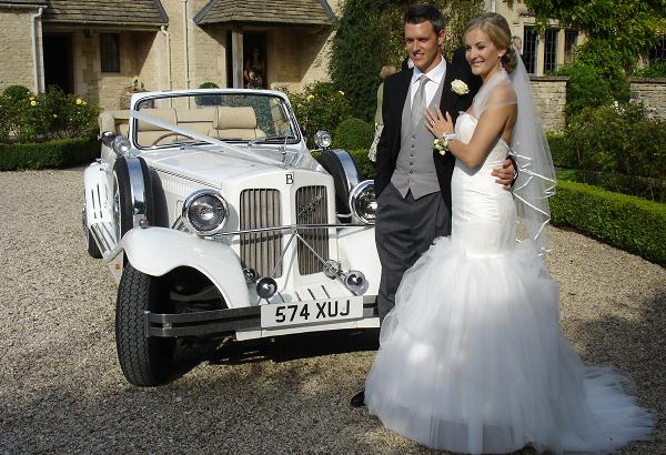 Spirit Wedding Cars | A bride and groom pose in front of a white car with a license plate that says 574 xuj