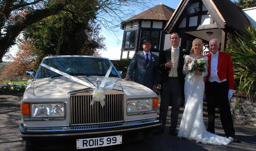 Spirit Wedding Cars | A bride and groom are posing for a picture in front of a wedding car.