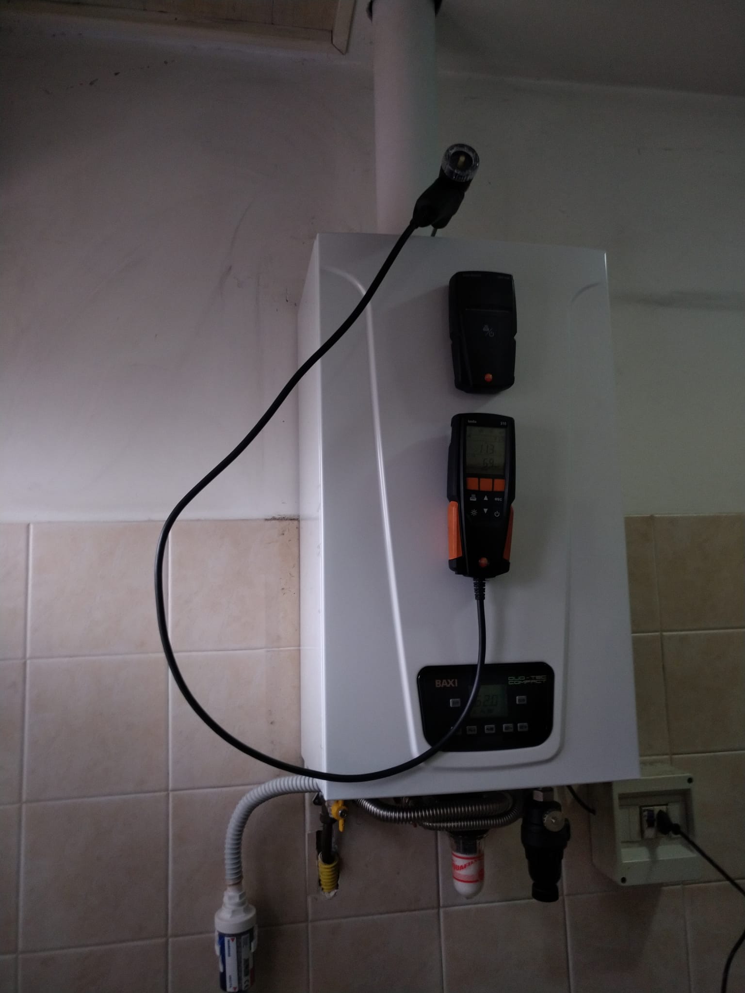 Quadro elettrico a parete con contatori e cavi a vista in un locale di servizio piastrellato.