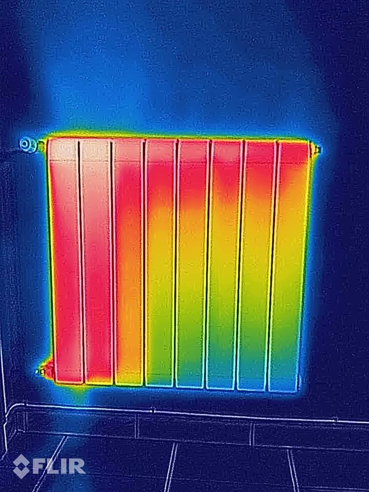 Immagine termica di un radiatore con la parte superiore rossa e calda e la parte inferiore blu e più fredda, sullo sfondo di una parete scura.