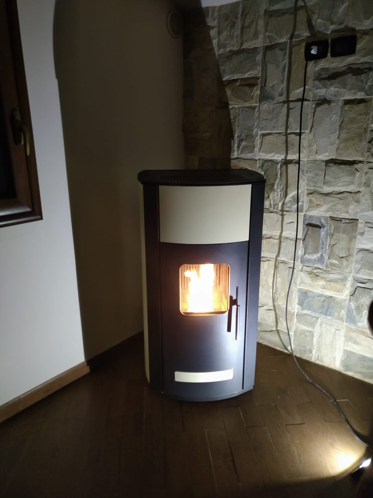Stufa a pellet accesa su un pavimento di legno scuro accanto a un muro di pietra in una stanza