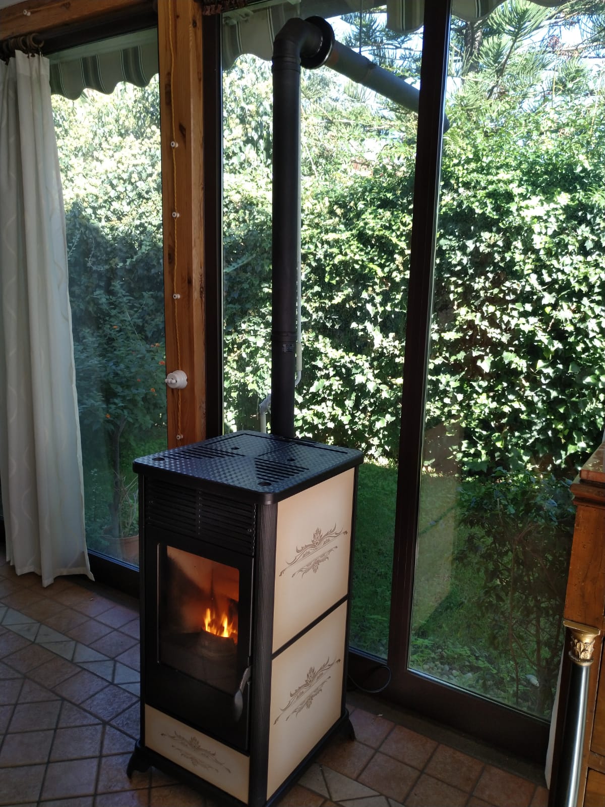 Stufa a legna con fuoco all'interno, vicino a una grande finestra che si affaccia sul verde.