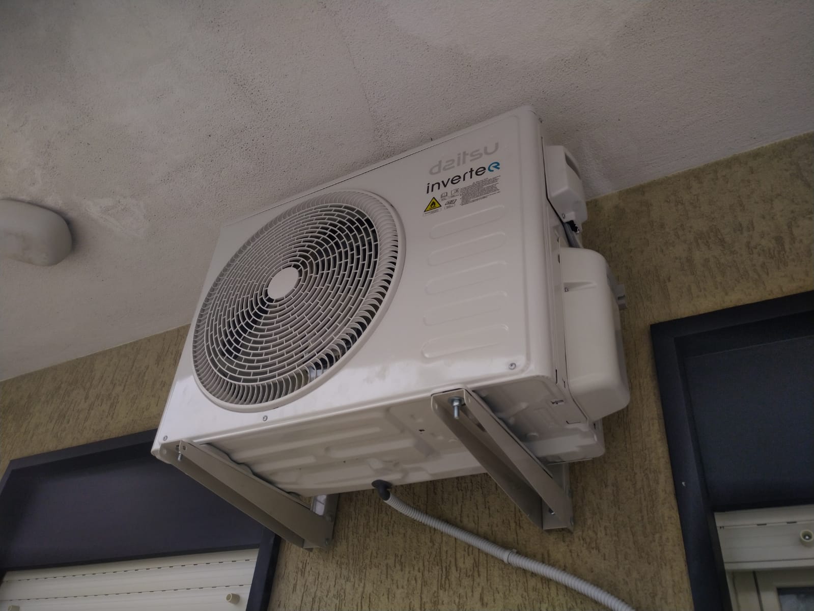 Condizionatore d'aria esterno a parete con grande ventola, installato su una facciata di edificio beige.